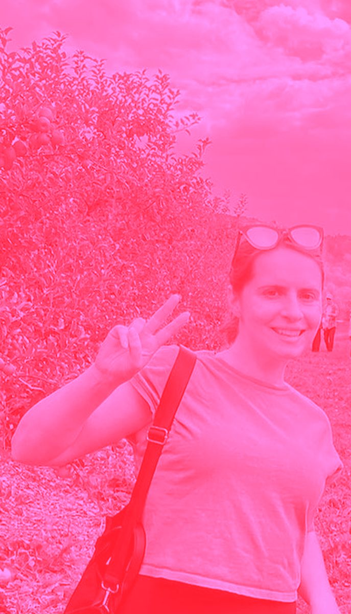 Jess Luszcz flashing a peace sign in a pink filtered photo.